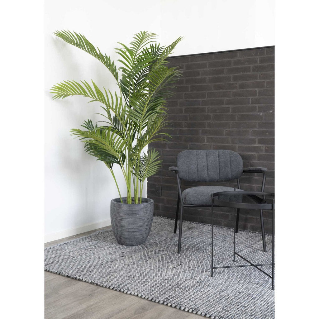 Potted plant next to a gray chair and small table against a brick wall.
