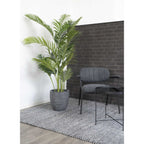 Potted plant next to a gray chair and small table against a brick wall.