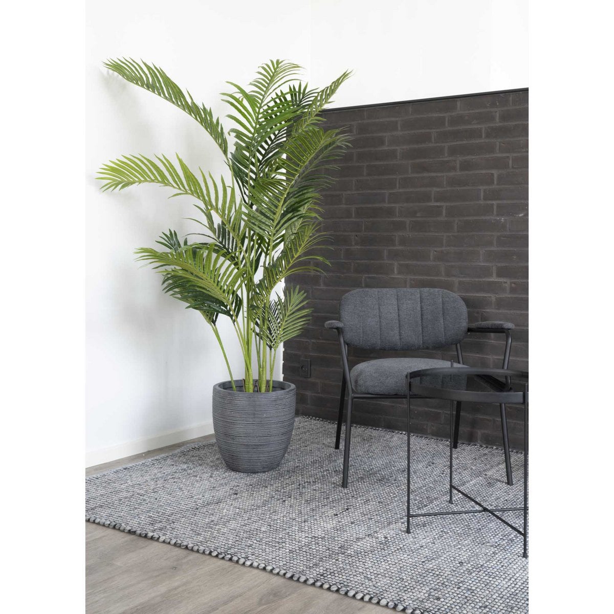 Potted plant next to a gray chair and small table against a brick wall.