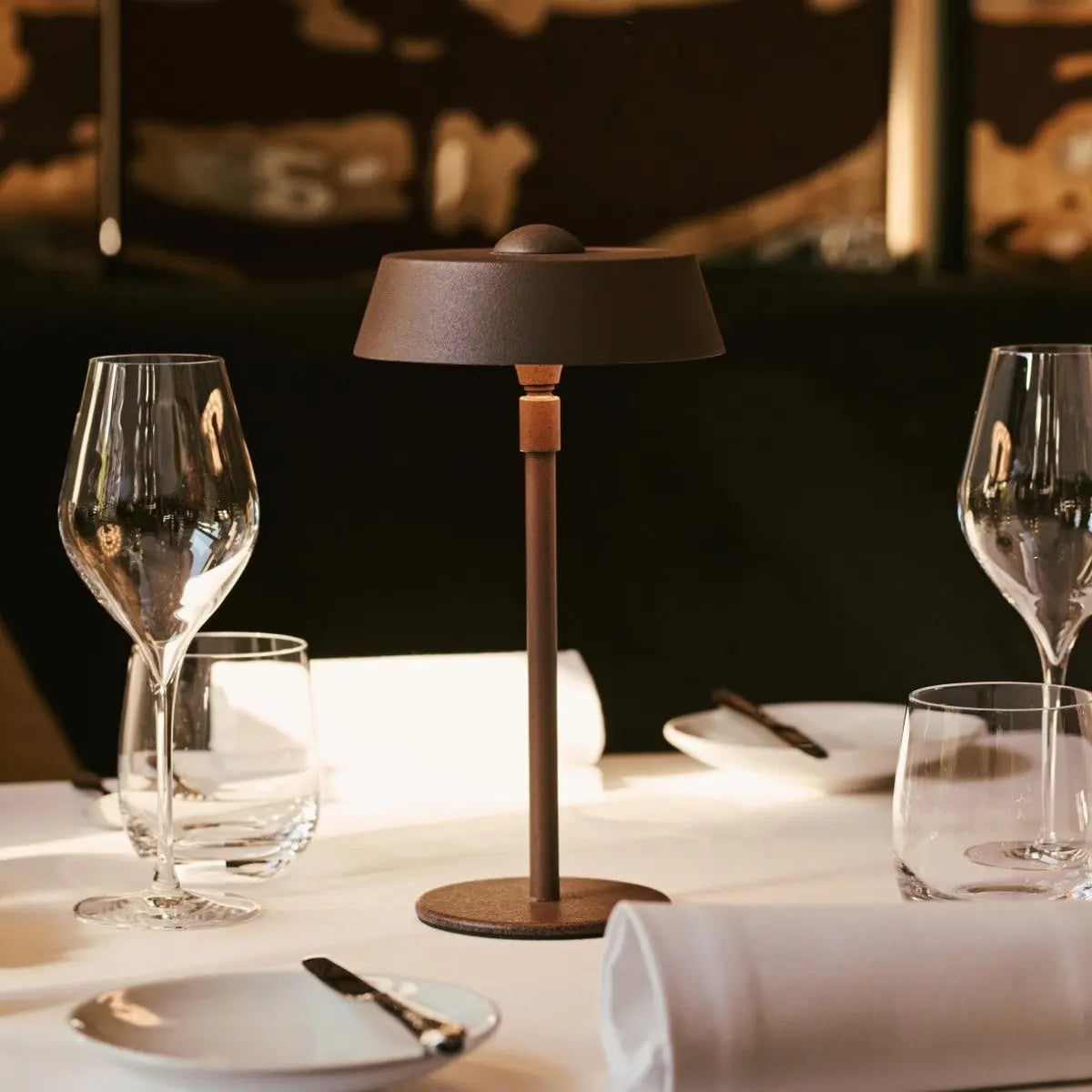 Dining table setting with wine glasses, lamp, and cutlery on a dark background