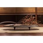 Decorative black dish with dried plants on a wooden surface, featuring the brand 'Oriental'.