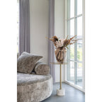 Round gray sofa with a vase of flowers on a small table in a room with large windows.