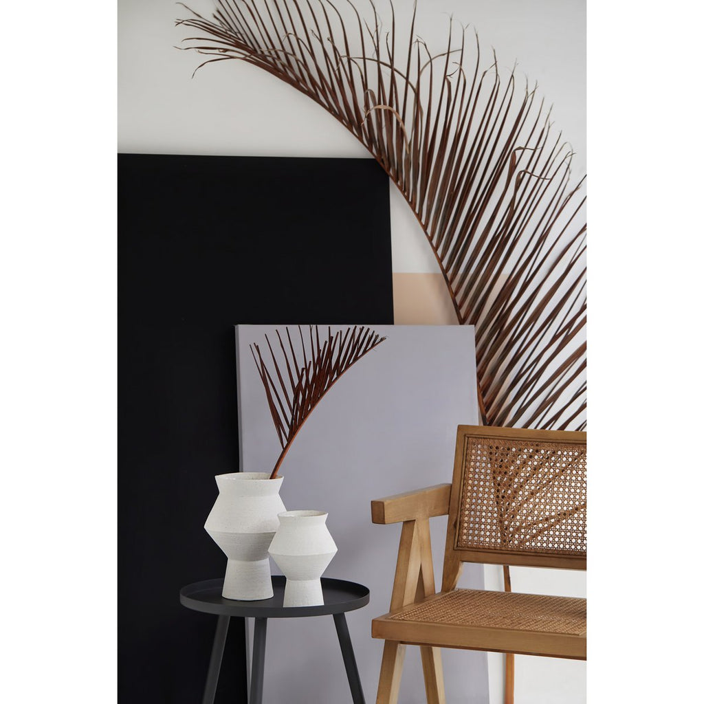 Decorative wall art with a large leaf design, white vases on a black table, and a wooden chair.