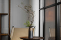 Decorative vase with branches on a table in a modern interior setting, featuring the brand 'Oriental'.