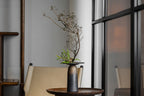 Decorative vase with branches on a table in a modern interior setting, featuring the brand 'Oriental'.