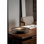 ULFUR ceramic flat bowl in bronze to black glaze on dark oak surface in warm Nordic-Japanese interior with bare branch