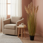 Tall artificial sorghum grass plant beside a sofa in a warm Nordic interior with soft natural light