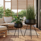 Set of two black steel Ardola plant pots on a sheltered balcony with warm afternoon light and rattan furniture