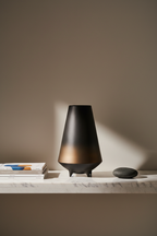 Tall bronze-to-black ceramic vase on a marble shelf with art books and a smooth stone