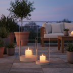 Set of two beige glass and metal hurricane candle holders on a sheltered terrace at dusk with warm candlelight