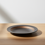Ulfur East+West flat ceramic plate on oak surface with soft daylight and clean off-white background