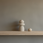 Segura beige stoneware sculptural vase on travertine shelf, concrete wall, straight-on