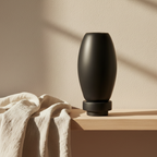 Matte black RUDAL microcement vase with oval body and stepped base styled on a Scandinavian shelf