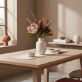 Realistic artificial King Protea bouquet in tall ceramic vase on a dining table in a warm Nordic interior