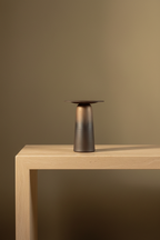 Bronze-to-black two-part ceramic architectural vase on a travertine console against a warm limewash wall