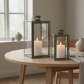 Set of two Corfu green steel and glass lanterns styled on a Scandinavian dining table with warm candlelight