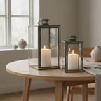 Set of two Corfu green steel and glass lanterns styled on a Scandinavian dining table with warm candlelight