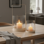 Set of two beige glass and metal hurricane candle holders styled on a Scandinavian dining table with warm candlelight
