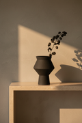 Black speckled ceramic vase on a travertine console against a warm limewash wall