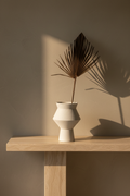 White speckled ceramic vase on a travertine console against a warm limewash wall