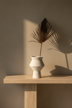 White speckled ceramic vase on a travertine console against a warm limewash wall
