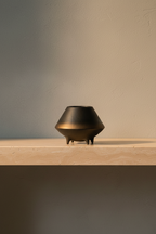 Bronze-to-black ceramic sculptural bowl on a travertine console against a warm limewash wall