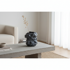 Black rock-look ceramic vase on concrete surface in a modern Nordic interior with a single dried stem