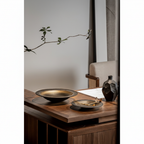 ULFUR ceramic flat bowl grouped with ULFUR vases on a dark oak sideboard in a warm moody interior