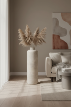 Tall antique beige metal Hou floor vase with dried pampas grass stems in a Nordic living room corner