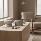 Set of two grey cement candle holders on a sideboard in a Nordic interior with pebbles and dried botanicals