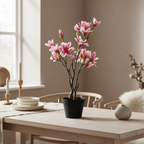 Tall slender realistic artificial magnolia tree on a dining table in a warm Nordic interior with soft natural light