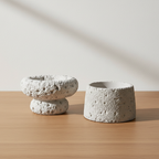 Set of two grey cement candle holders on oak surface with soft daylight and clean off-white background